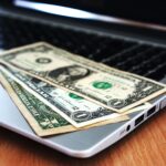 Banknoty dolarowe leżące na klawiaturze laptopa