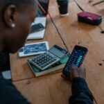 Uczeń trzyma smartfon nad biurkiem, obok leży kalkulator