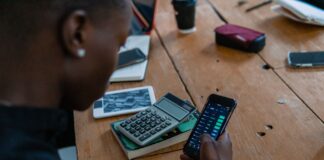 Uczeń trzyma smartfon nad biurkiem, obok leży kalkulator