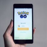 Dłoń trzyma smartfon z ekranem logowania do aplikacji Pokémon Go