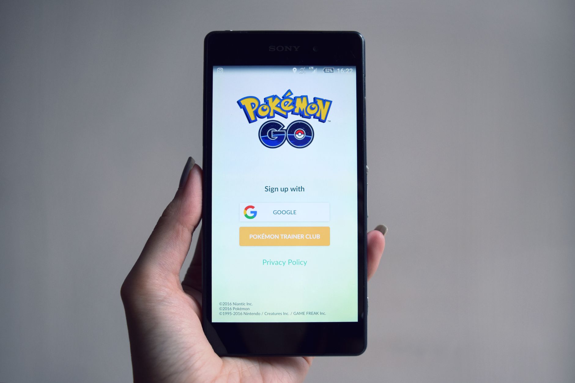 Dłoń trzyma smartfon z ekranem logowania do aplikacji Pokémon Go
