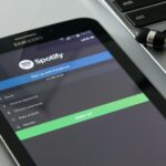 Smartfon z ekranem logowania Spotify obok laptopa i słuchawek