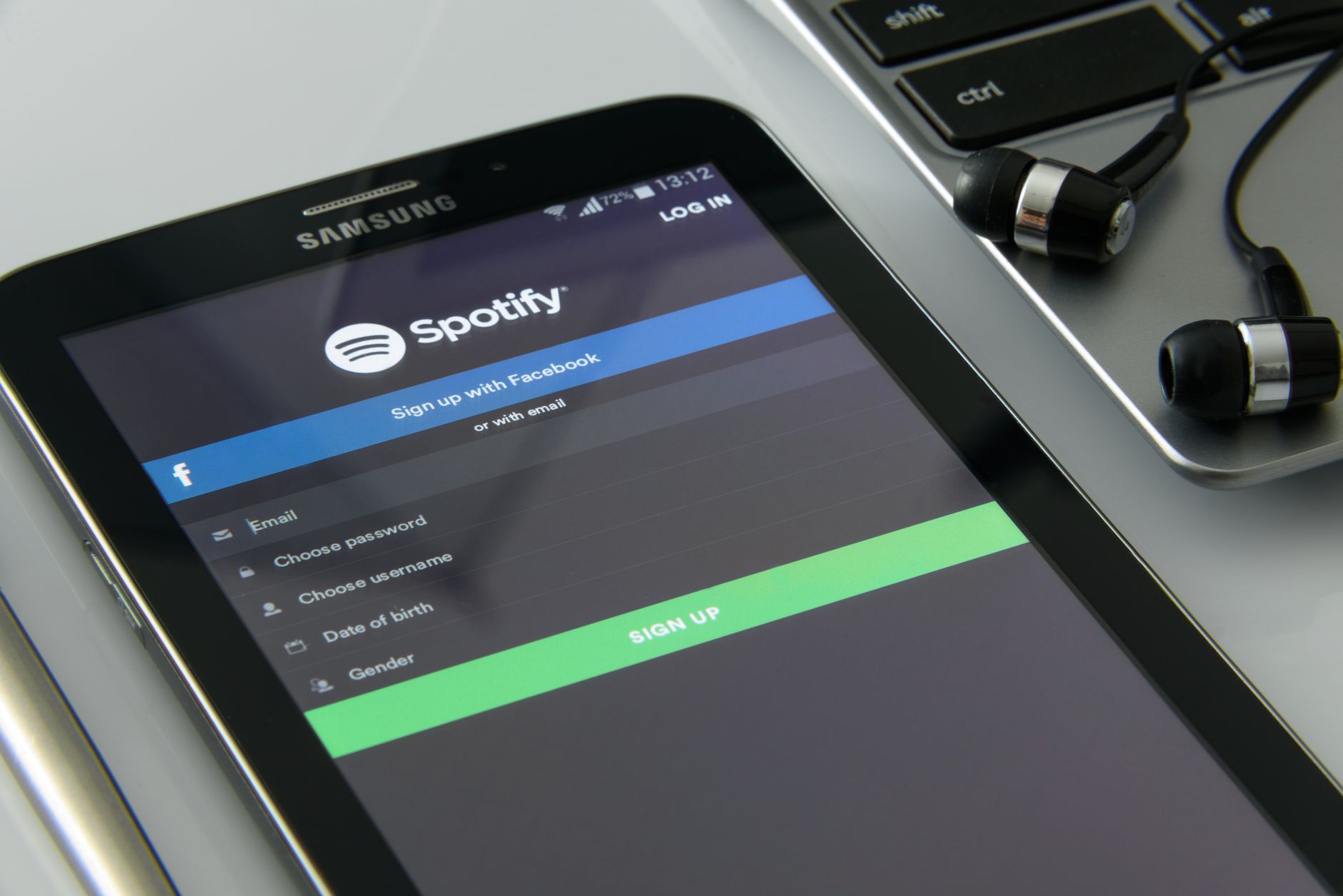 Smartfon z ekranem logowania Spotify obok laptopa i słuchawek
