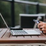 Mężczyzna korzysta z internetu w telefonie przy laptopie w kawiarni