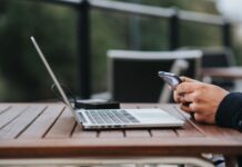 Tethering z telefonu czy modem LTE? Najlepszy sposób na internet w podróży Mężczyzna korzysta z internetu w telefonie przy laptopie w kawiarni