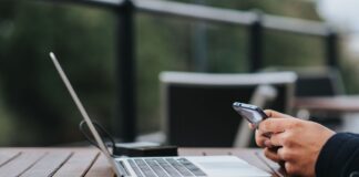 Mężczyzna korzysta z internetu w telefonie przy laptopie w kawiarni