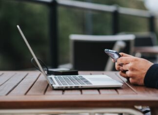 Mężczyzna korzysta z internetu w telefonie przy laptopie w kawiarni