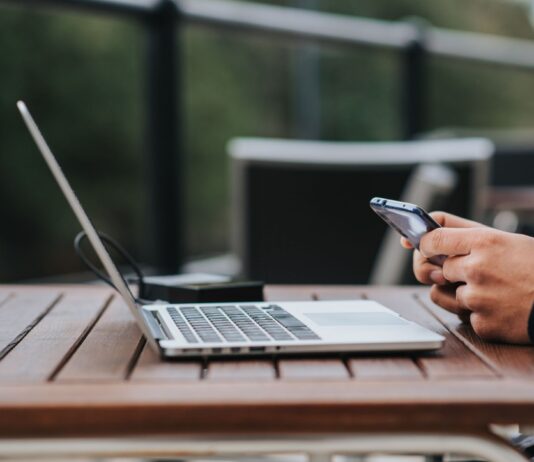 Mężczyzna korzysta z internetu w telefonie przy laptopie w kawiarni