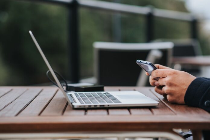 Mężczyzna korzysta z internetu w telefonie przy laptopie w kawiarni Mężczyzna korzysta z internetu w telefonie przy laptopie w kawiarni