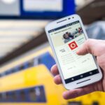 Osoba korzysta ze smartfona na peronie z przejeżdżającym pociągiem