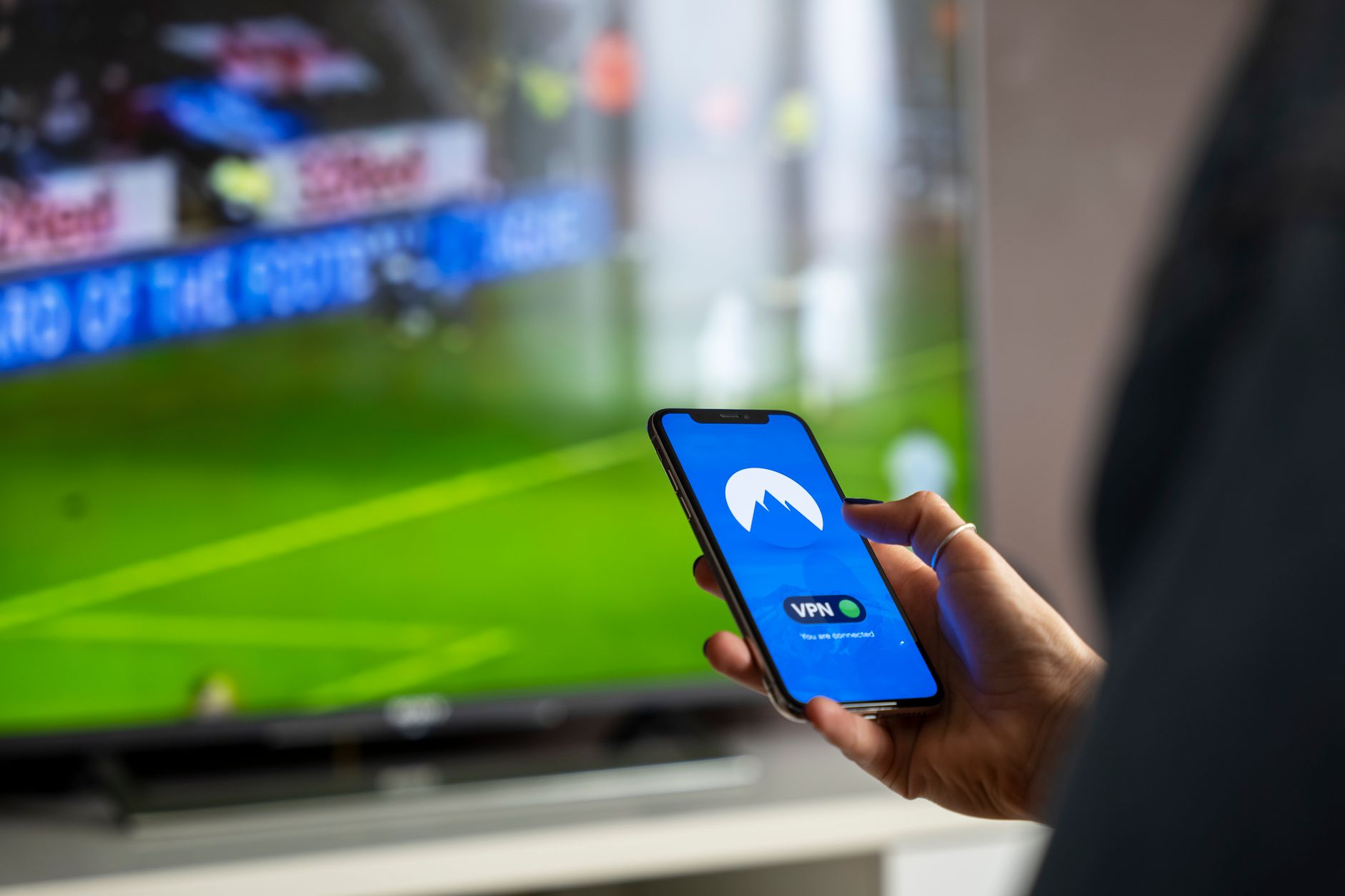 Osoba trzyma smartfon z aplikacją VPN podczas oglądania sportu w TV