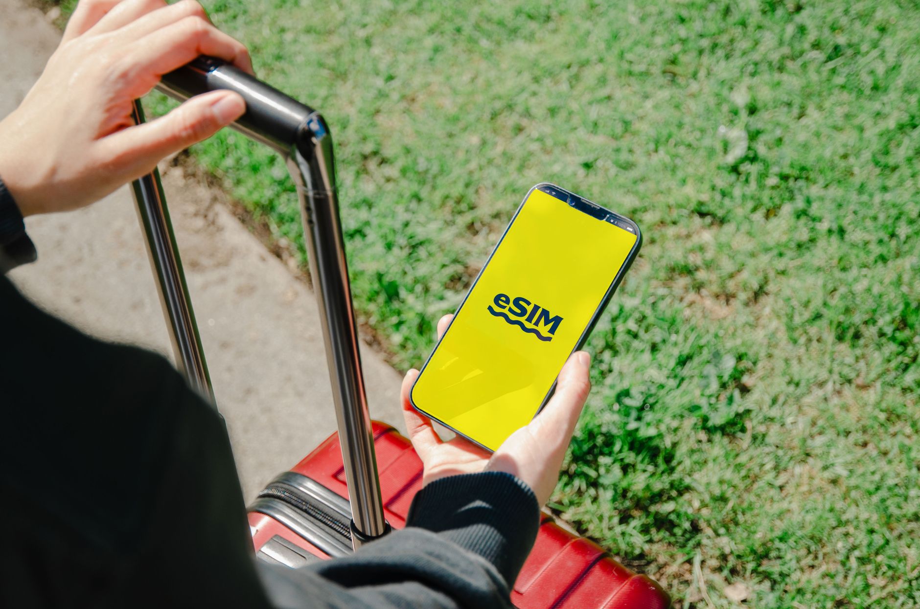 Osoba z walizką sprawdza aplikację eSIM na smartfonie na ulicy